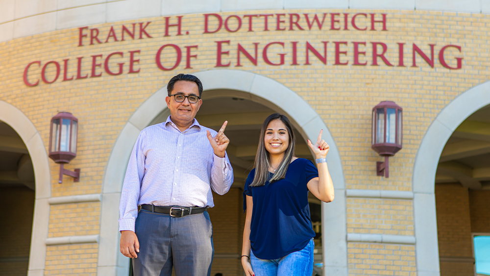 Dr. David Ramirez and Janay S. Garza form the letter “J” with their left hands. In the background, words read: Frank H. Dotterweich College of Engineering.
