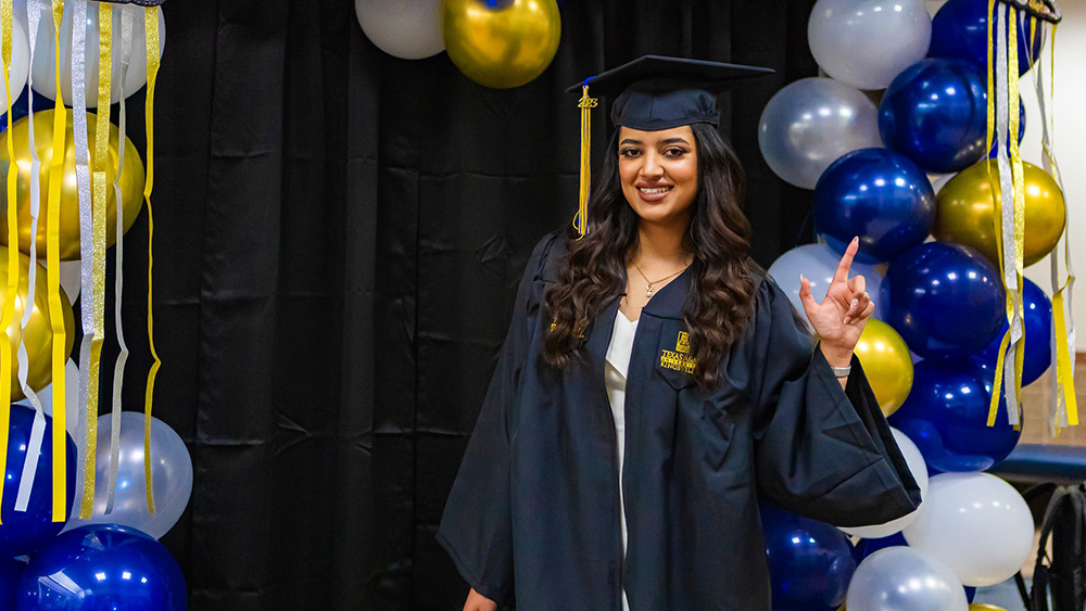 A graduate smiles toward the camera while creating a "J" with her hand.