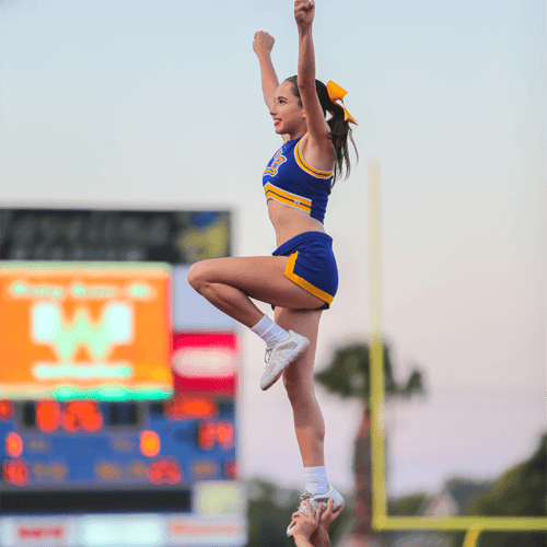 Cheer member performs stunt at football game.