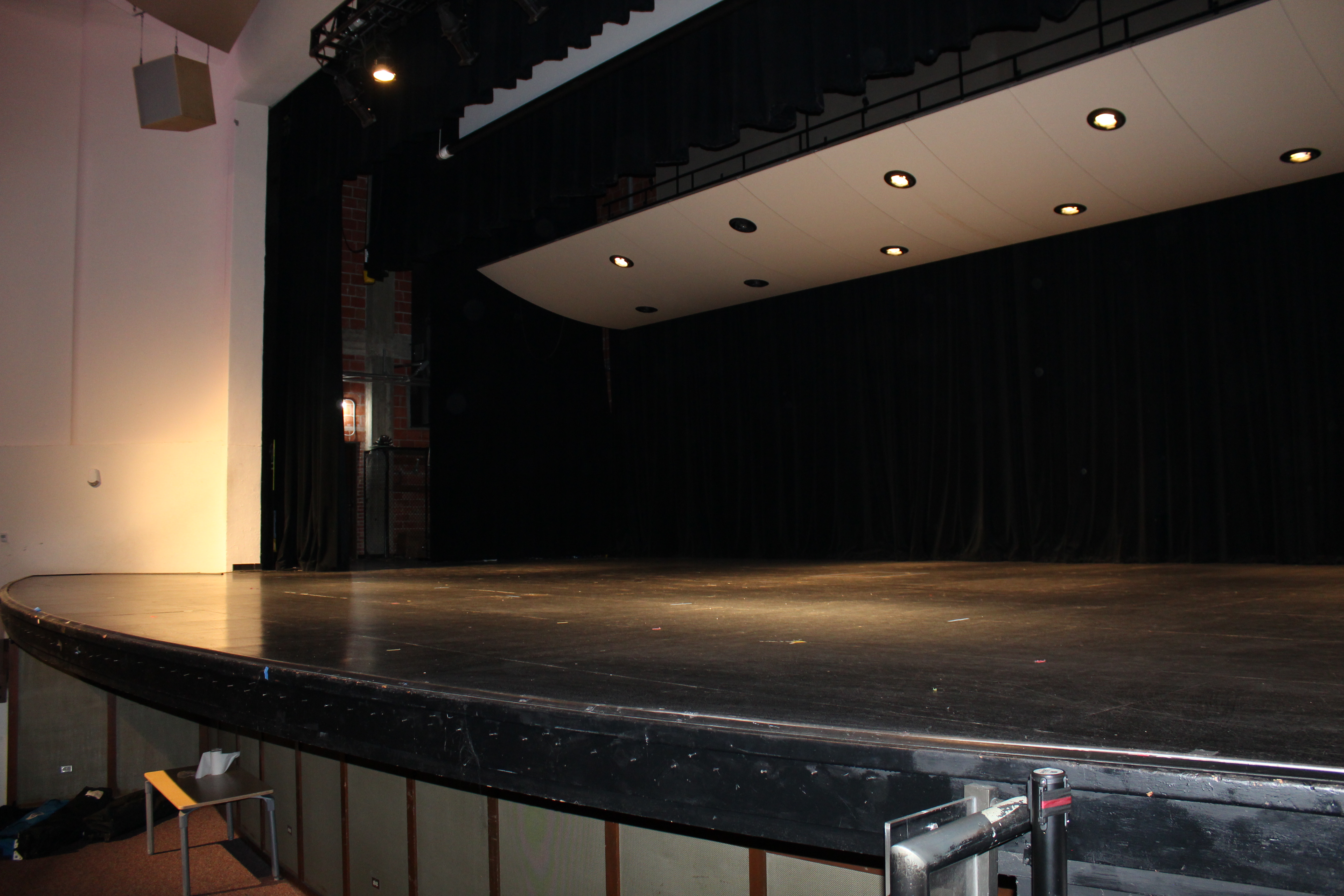 An image of the stage of the auditorium, featuring ceiling hung lighting that covers the stage and black curtains.