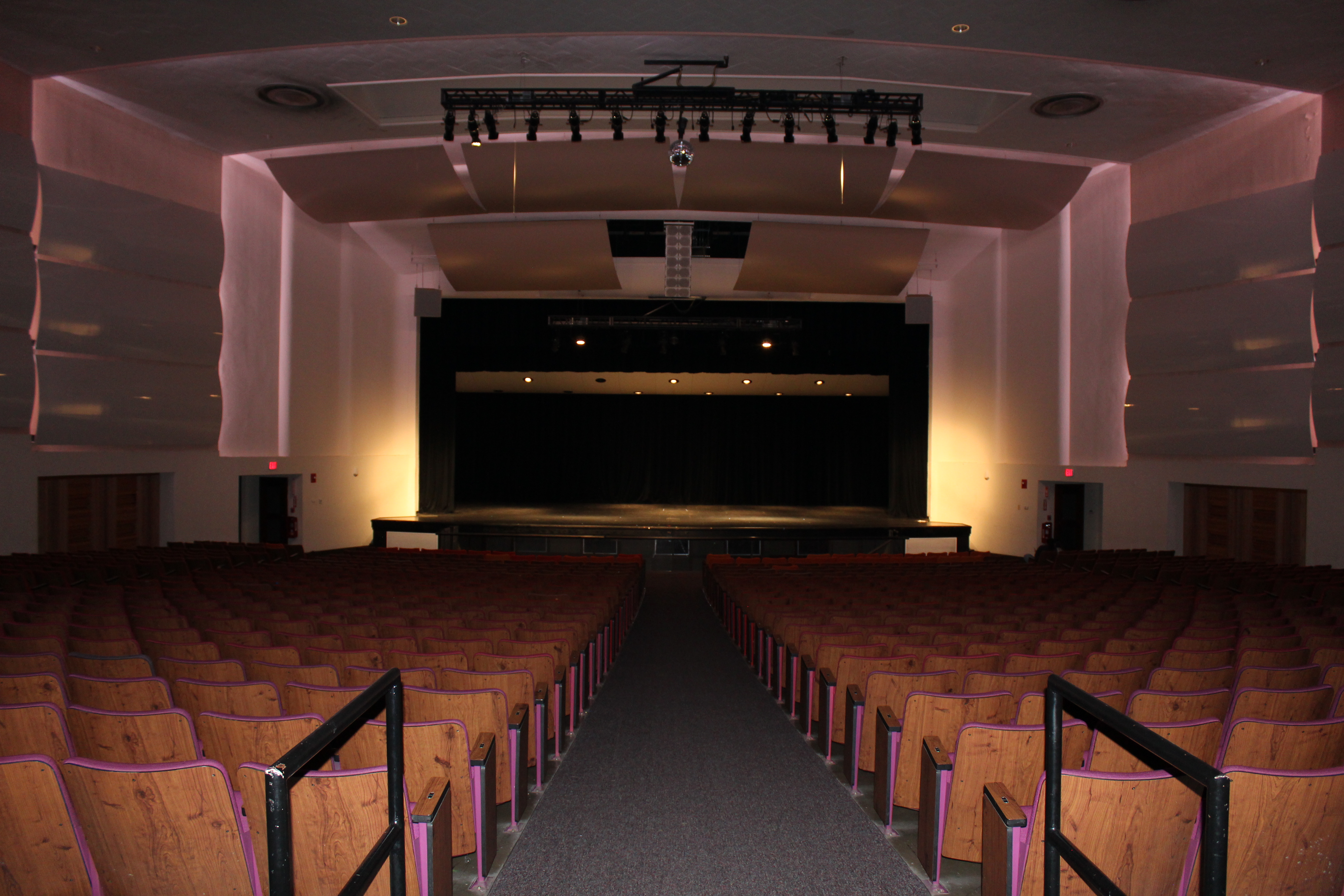 A picture of a large auditorium from the back of the seating area, facing a large, empty stage.
