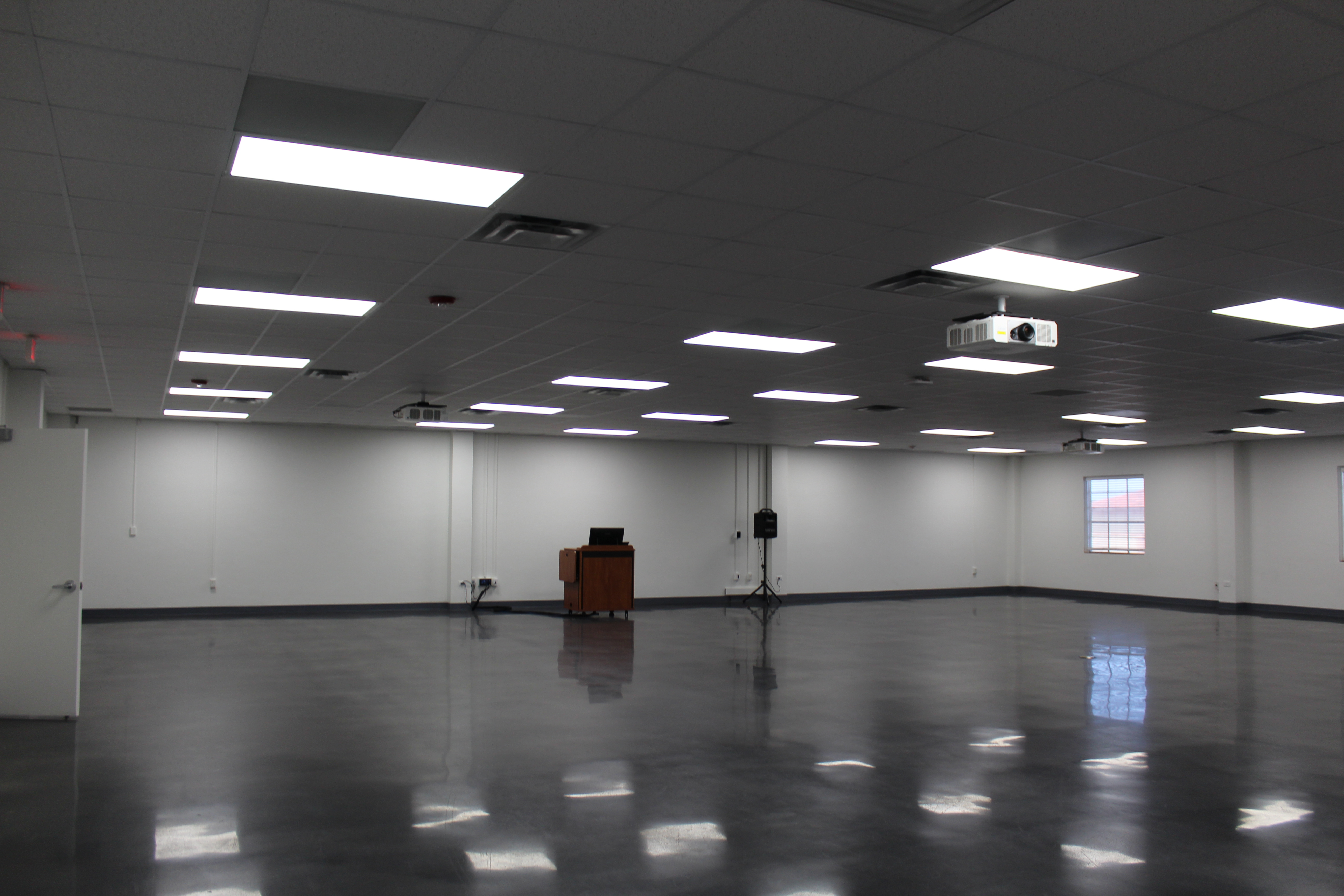 Room 219 has white walls, a brown wood podium, and blue-grey epoxy flooring.