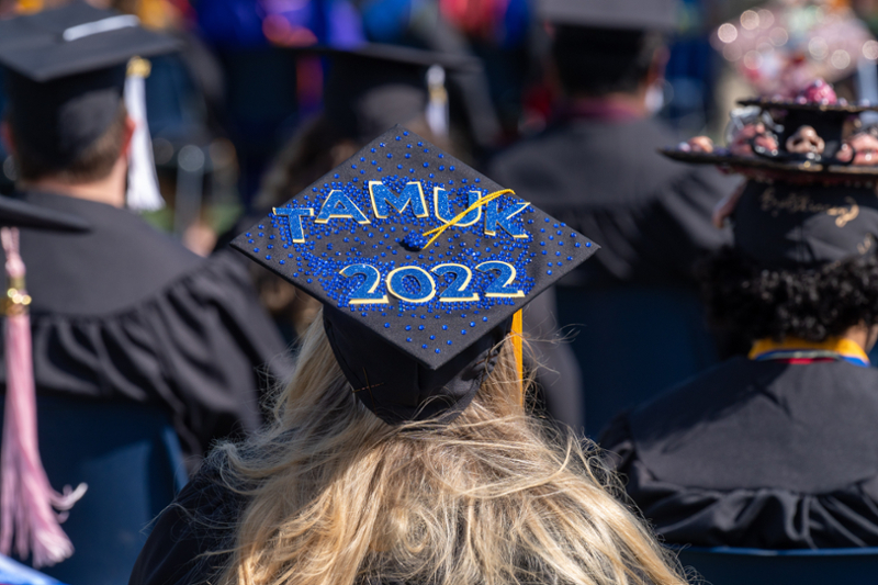 Spring 2022 graduate sitting at graduation with "2022 TAMUK" on their graduation cap.