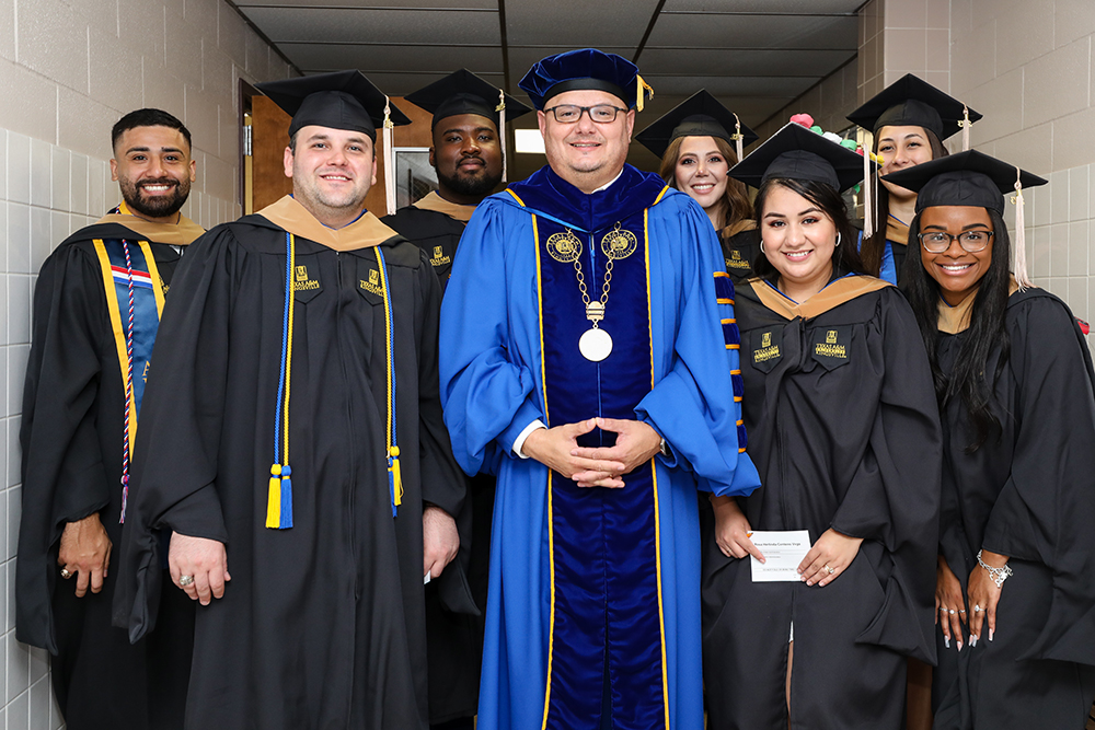 Texas A&M University-Kingsville President Dr. Robert Vela Jr. stands surrounded by seven prospective graduates ahead of the Summer 2023 graduation ceremony.