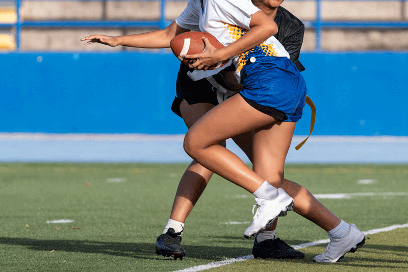 Women's flag football player in blue shorts runs past a defender in black shorts.
