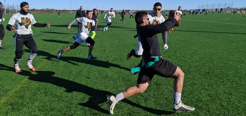 A student holding the football dips to avoid getting his flags pulled.