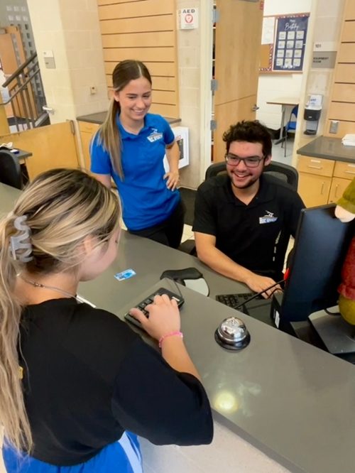 Two student employees assisting a student at the front desk